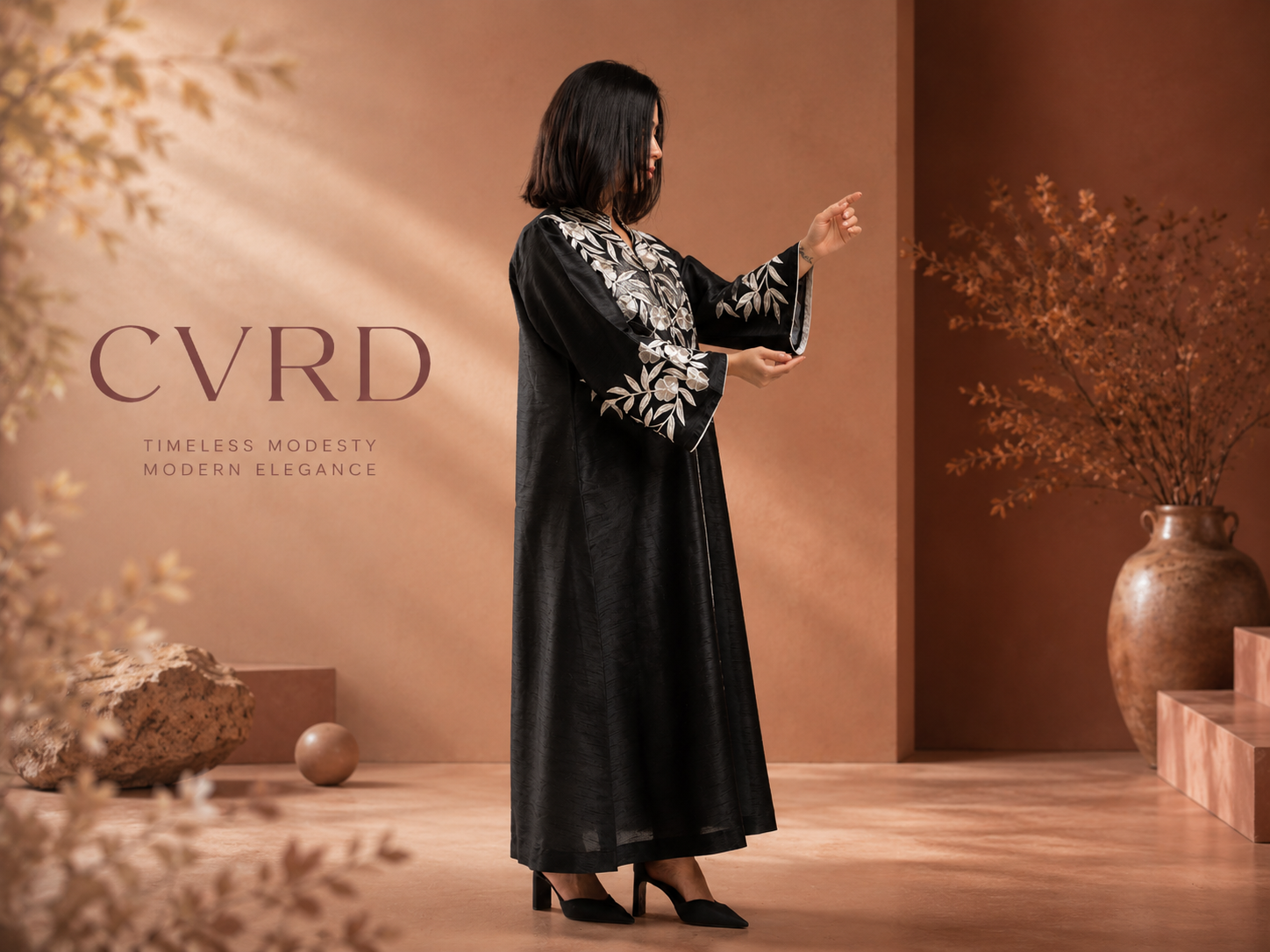 Woman in a black dress with white embroidery standing in a warm-toned room with 'CVRD' branding.